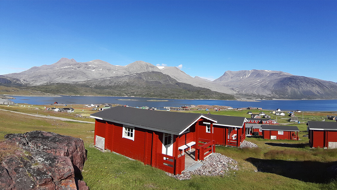 Igaliku Bygdehotel: Mange røde hytter med udsigt over fjord og bjerge.