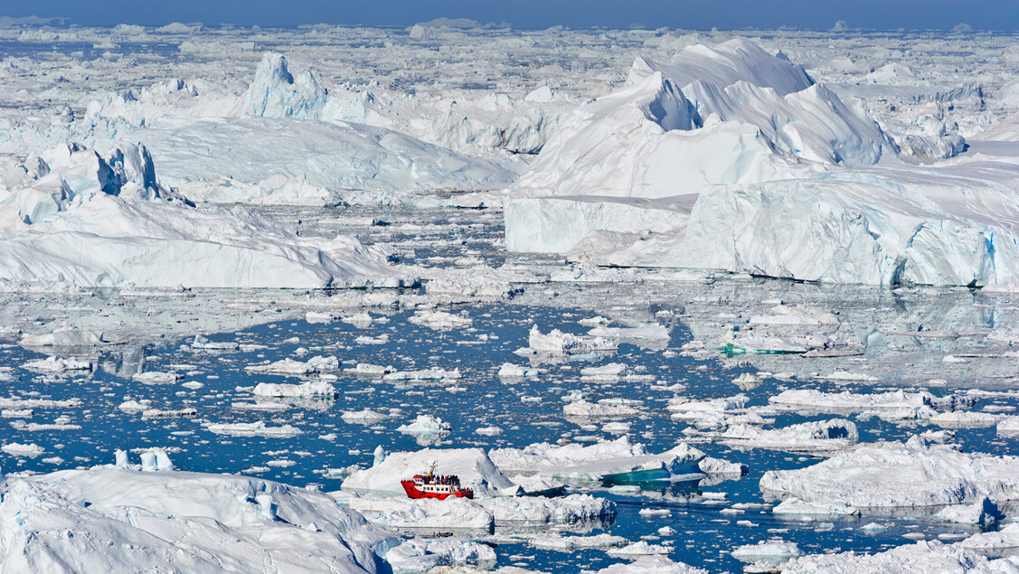 Rød og hvid Disko Line-færge sejler blandt gigantiske isbjerge i Diskobugten.