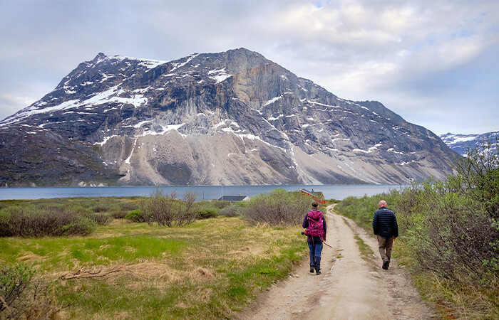 Two people walking in the beautiful nature with fjord in the background.