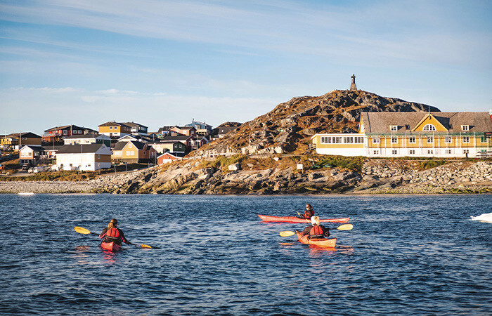 3 people in each kayak in the ocean, with a beautiful view of the city.