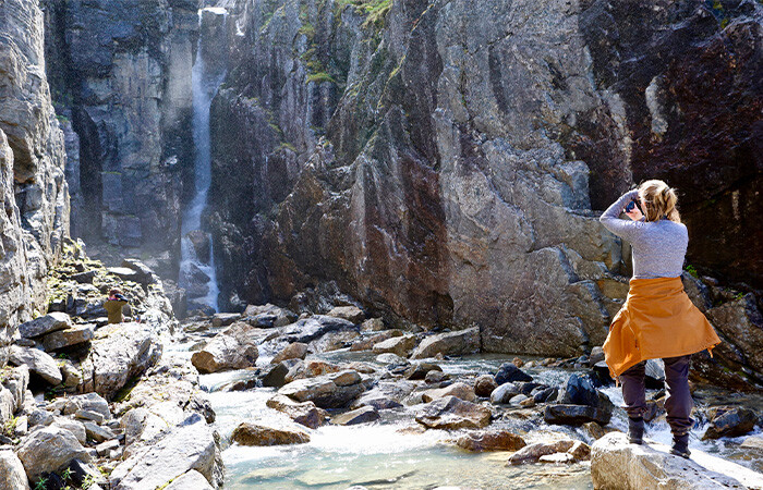 A woman taking a picture of the beautiful waterfall.